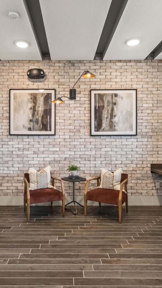 a modern office with a brick wall and wooden desk at The La Ventana at Canyon West Apartments